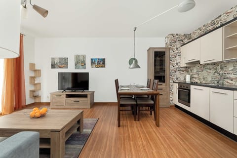 A spacious open-plan living room with a dining table, kitchen, and access to natural light from large windows.