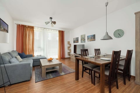A dining and seating area featuring a wooden table, modern light fixture, and large windows letting in daylight.

