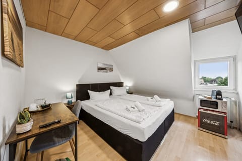 Gemütliches Doppelzimmer unterm Dach mit Boxspringbett, Arbeitsbereich und kleiner Pantry mit Kaffeemaschine und Mikrowelle – ideal für kurze Aufenthalte.