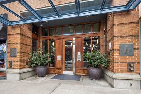 Secure entry with stylish brick architecture, potted greenery, and a glass canopy welcoming you to the building.