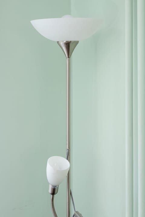 A tall white floor lamp standing against a clean, pastel-colored wall.