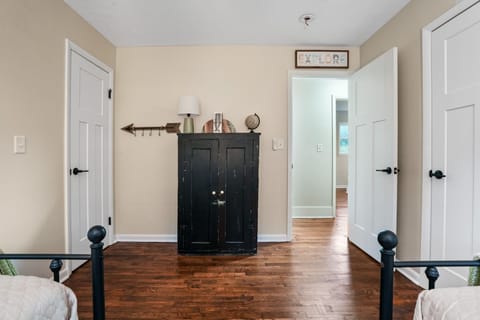 This comfy bedroom has twin beds, warm wood floors, and a rustic dresser with simple décor. Neutral colors and soft lighting make it a relaxing space that’s perfect for winding down and getting a good night’s rest.
