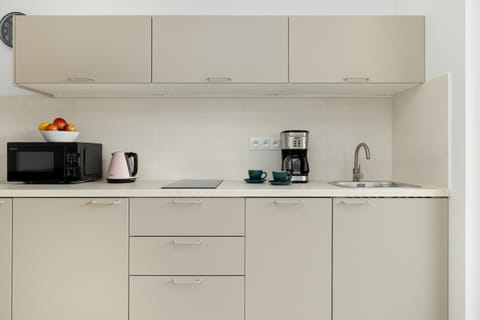 Another view of the compact kitchen corner featuring basic appliances, white cabinets, and sleek countertops.