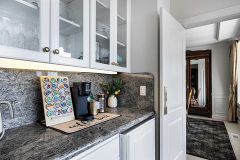 Barista-ready coffee bar - marble counter with premium machine, capsule display, and glass-front cabinets showcasing crystal stemware.