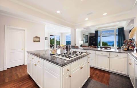 Cook with a view - bright white kitchen featuring gold accents, gas range, and windows framing water vistas.