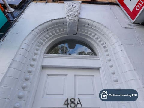A white, ornate arched doorway with intricate detailing above a double door numbered 48A. The door features a semi-circular window and is part of a classic architectural facade. The photo is taken from a low angle.