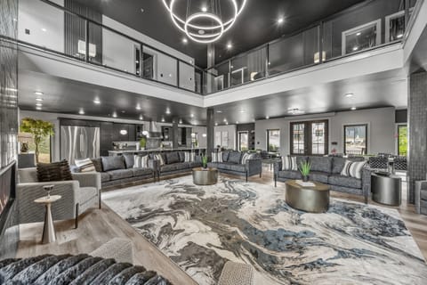 Airy, open-concept living room designed for gathering and relaxation, featuring a massive gray couch with additional seating for up to 34 guests, an elegant chandelier, and floor-to-ceiling glass views.