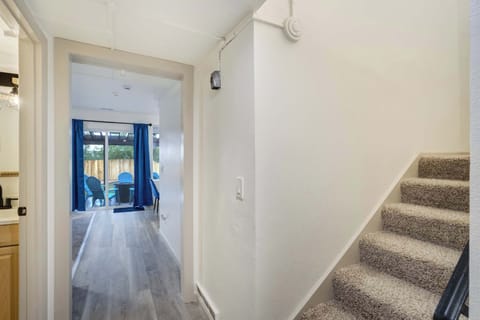 Inviting stairwell with plush carpet, a decorative black railing, and a statement wall clock accented by a modern chandelier. The window fills the space with daylight, creating a bright transition between floors.