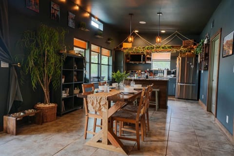 Enjoy meals and conversations at a spacious wooden dining table, surrounded by modern, nature-inspired touches and a view of the well-equipped kitchen.