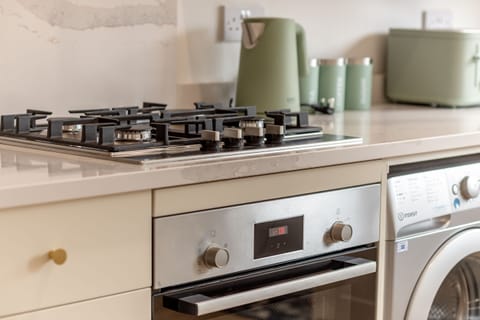 Stainless steel gas hob and oven on a marble countertop beside green kitchen accessories and washing machine.