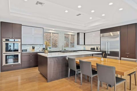 With top-of-the-line appliances and ample cabinetry, this kitchen perfectly blends function and elegance. The six-seater wooden dining table, white ceilings and walls, and wood-finish floors add warmth and style to the space.