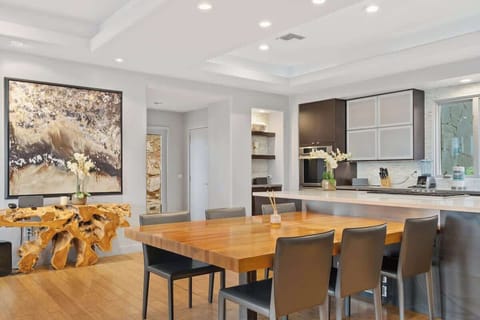 This kitchen is fitted with top-of-the-line appliances and generous cabinetry, a wood-finish dining table, live-edge console table with a delicate orchid plant, and artwork highlighted by pin lights complete the sophisticated, modern space.