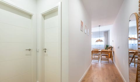 Well-lit hallway with warm wooden flooring and white doors leading to the dining area. Framed artwork on walls and clean architectural lines showcase the apartment's contemporary design and attention to detail.