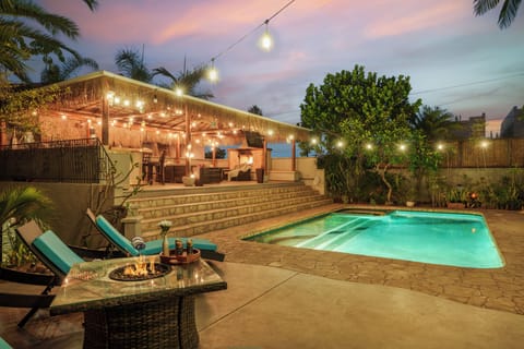 Tropical backyard oasis with a glowing pool, fire pit, tiki-style cabana, and dreamy sunset skies.