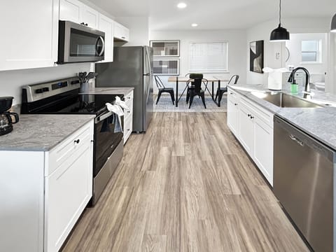 Your fully-equipped kitchen opens seamlessly to a bright dining area, where modern white cabinets and marble countertops create the perfect space for cooking memorable meals during your stay.
