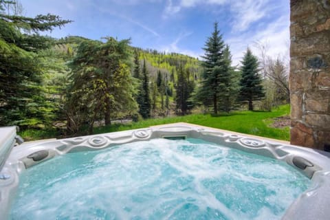 Indulge in the tranquil embrace of nature while soaking in the bubbling hot tub, framed by lush pine trees and a serene landscape that invites relaxation.