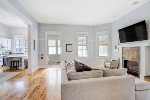 A bright living room with a stone fireplace, mounted Smart TV, and wraparound windows creates a relaxing space to gather after a day outdoors.