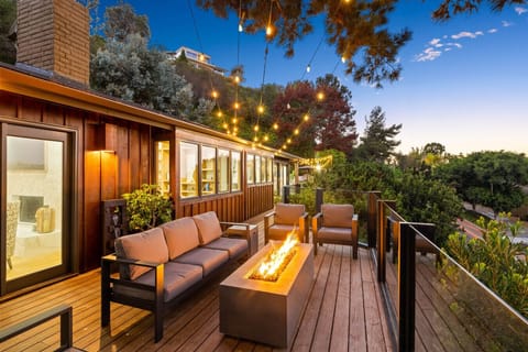 A glowing hillside deck with a modern fire pit and cozy seating offers the perfect spot to unwind under magical string lights and treetop views.