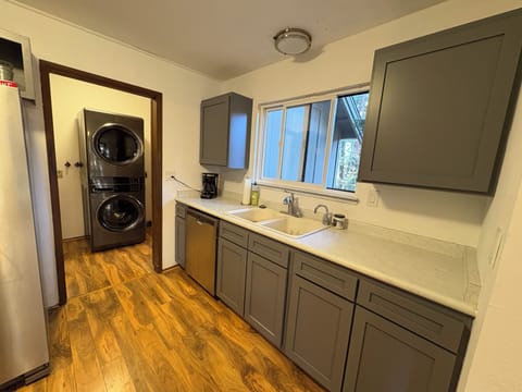 Modern kitchen with gray cabinets and white countertops, featuring easy access to in-unit laundry facilities through the adjoining room.