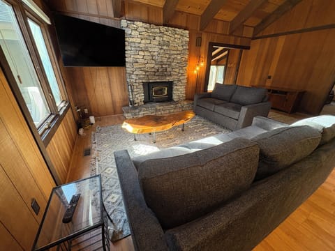 Relax in this cozy living room featuring comfortable seating, a stone fireplace, and vaulted wood ceilings that create the perfect mountain retreat atmosphere.
