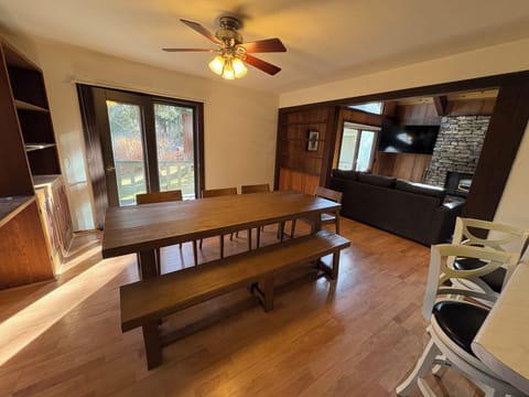 Gather around the rustic wooden dining table with bench seating, perfect for memorable meals with your group. The stone fireplace and ceiling fan create a cozy mountain lodge atmosphere.