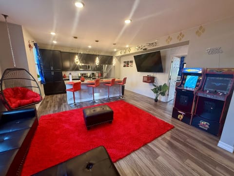 Relaxed hangout space with soft seating, a hanging chair, & a big TV, all connected to a modern kitchen with an island & bar stools. Classic arcade games add extra fun for guests of all ages.