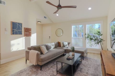 Open-concept living, dining, and kitchen area — bright, airy, and perfect for relaxing or entertaining. Living room features Crate & Barrel media console, 75-inch smart TV with Bose soundbar, and West Elm couch with ottoman.
