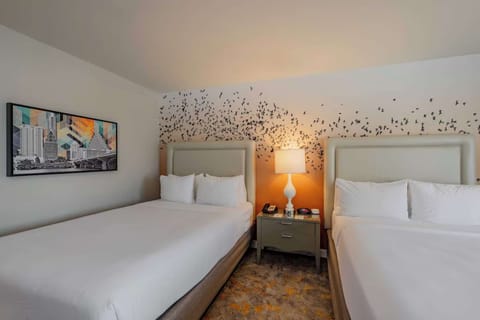 Bright room with two queen beds, bird mural, and soft wall lamp