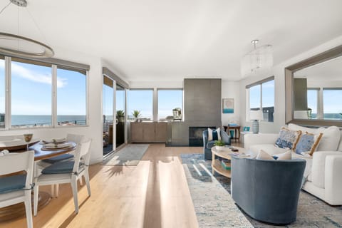 Light filled open living and dining area with expansive windows, ocean views, and direct access to the outdoor deck.
