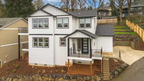 Modern two-story home featuring white siding, dark trim, and covered front porch in quiet residential neighborhood.