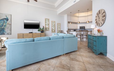 The living space features a cozy blue sofa, a large TV, and a stylish kitchen with bright decor and inviting seating