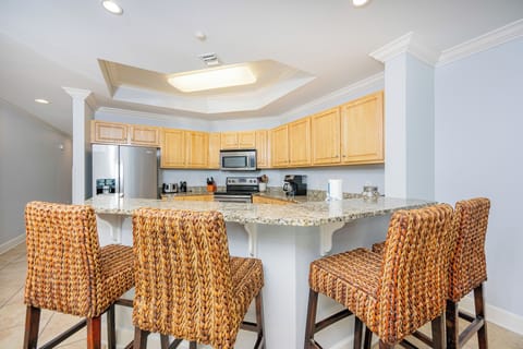 Bright kitchen with granite countertops, stainless appliances, and stylish woven barstools for casual dining