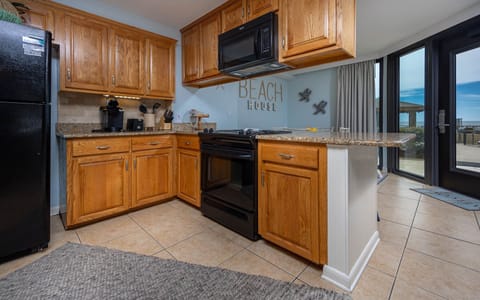 The kitchen features warm wood cabinetry, a black refrigerator, and a breakfast bar, with a view of the outdoor patio beyond