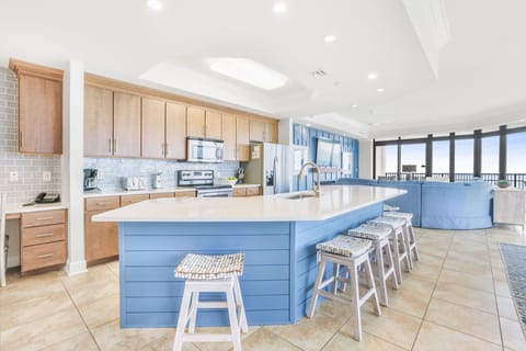 The kitchen features sleek modern appliances, a spacious blue island with seating, and a costal vibe to compliment your stay