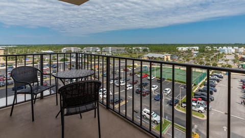 Master balcony featuring a round table and chairs, offering a view of nearby tennis courts and a vibrant parking area below