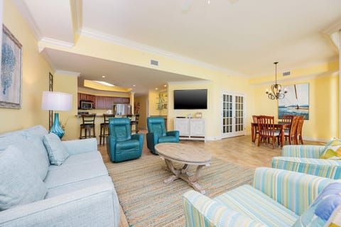 This living area features turquoise chairs, a cozy couch, a large TV, and a dining space with a nautical-themed painting