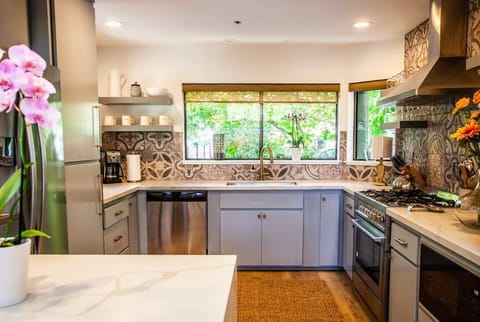 Bright, modern kitchen featuring sleek countertops, stainless appliances, and a stylish patterned backsplash. Large windows bring in natural light, creating a warm and inviting space perfect for cooking and gathering.