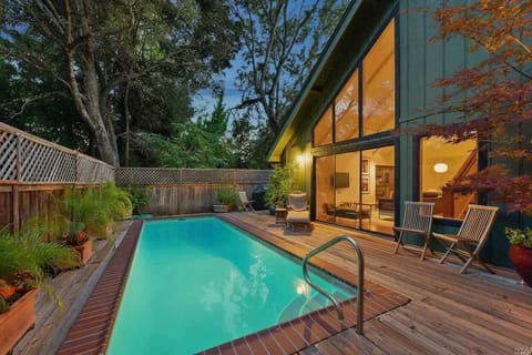 Peaceful private pool oasis surrounded by lush trees and warm wood decking. Floor-to-ceiling windows connect the indoors and outdoors, creating the perfect spot for a refreshing swim or evening relaxation.