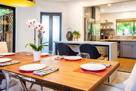 A welcoming dining area with a spacious wood table, elegant place settings, and natural light. Overlooks a modern kitchen, creating the perfect setup for cooking, hosting, and relaxing with family or friends.