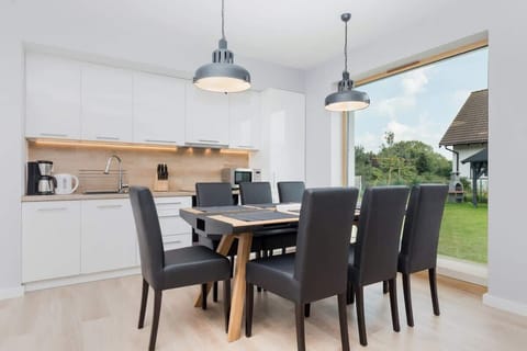 A bright dining area featuring a dark wood table with six black chairs, illuminated by modern pendant lighting, and complemented by large windows bringing in natural light.