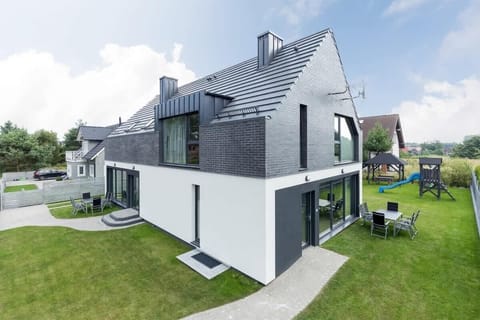 The exterior of a modern home with a gray and white facade, well-maintained greenery, and a spacious outdoor seating area, giving a clean and elegant appearance.