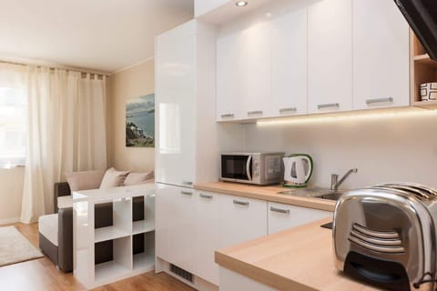  A sleek, modern kitchenette with white cabinets, integrated appliances, and light wood floors. A small dining table with chairs is nearby.