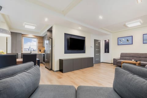 A modern living room with gray, comfortable couches, a flat-screen TV, and large windows offering a view outside.