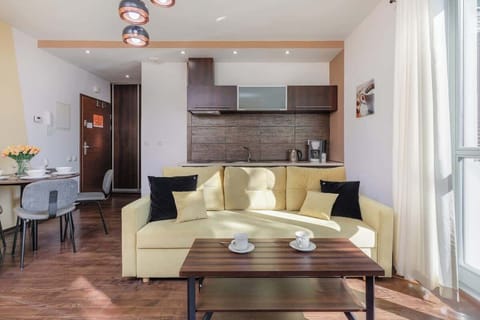 An open-plan living room and kitchen area with cream sofas, a dining table, and wooden cabinets, combining functionality and comfort.