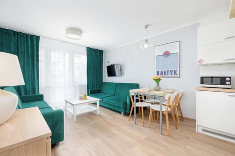 A living room decorated with coastal-themed artwork, a green sofa, and a simple wooden dining table.