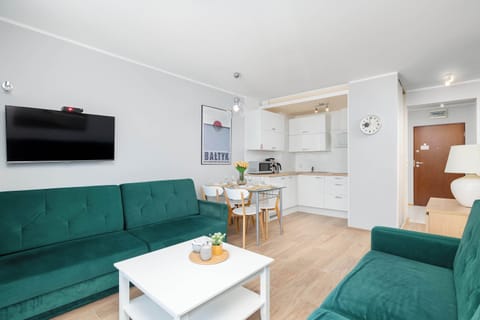 A well-lit living room featuring a green sofa, white furniture, and floor-to-ceiling windows.