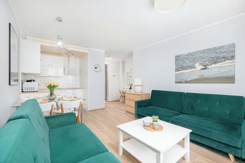 A compact space with a green sofa, a dining table, and a small kitchen area in the background.