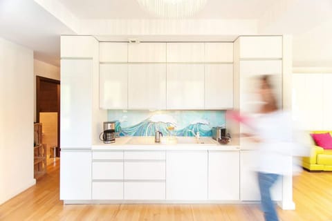 A bright, open kitchen with white cabinetry and a central island. The space has a light and airy feel, with a pop of color from the blue backsplash.