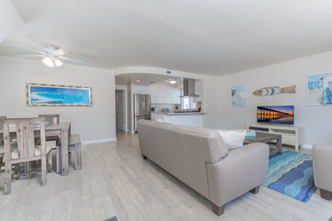 Vantage point from the unit's entry area toward kitchen, living room and TV. Wood-look tile flooring throughout updated living areas.