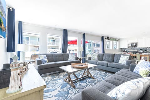 The main living area includes a sofa/loveseat set, side seating, cable TV, and a sliding glass door that opens to expansive front ocean view patio.